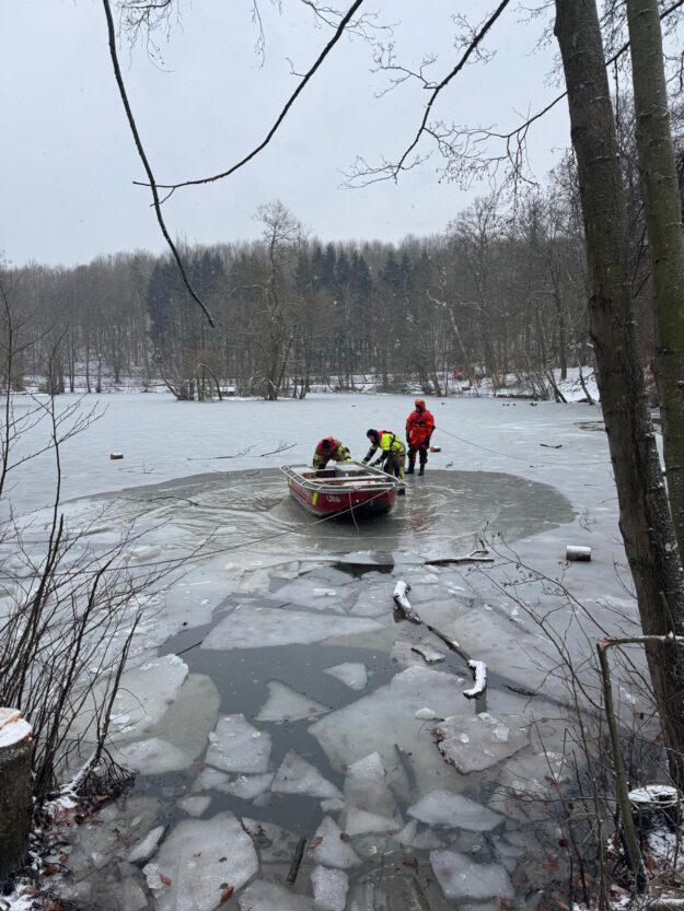 Drei Feuerwehrleute mit einem Boot in einem Wasserloch eines ansonsten zugefrorenen Sees