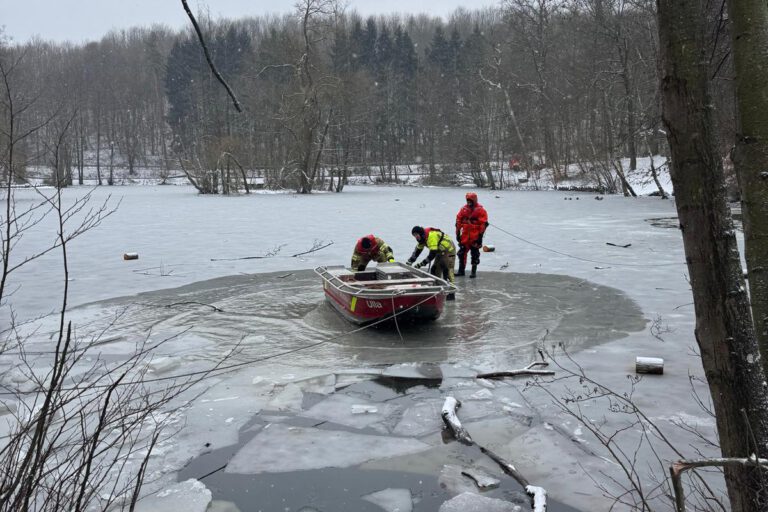 Drei Feuerwehrleute mit einem Boot in einem Wasserloch eines ansonsten zugefrorenen Sees