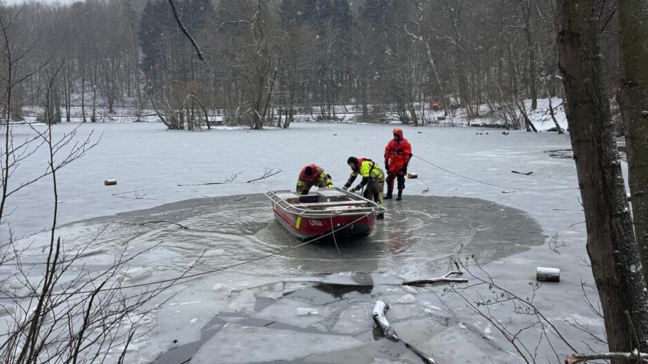 Drei Feuerwehrleute mit einem Boot in einem Wasserloch eines ansonsten zugefrorenen Sees