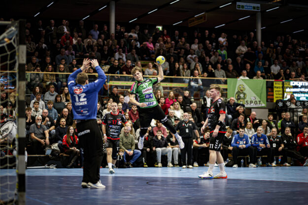 Ein Spieler des HTV beim Sprungwurf vor vollbesetzten Tribünen