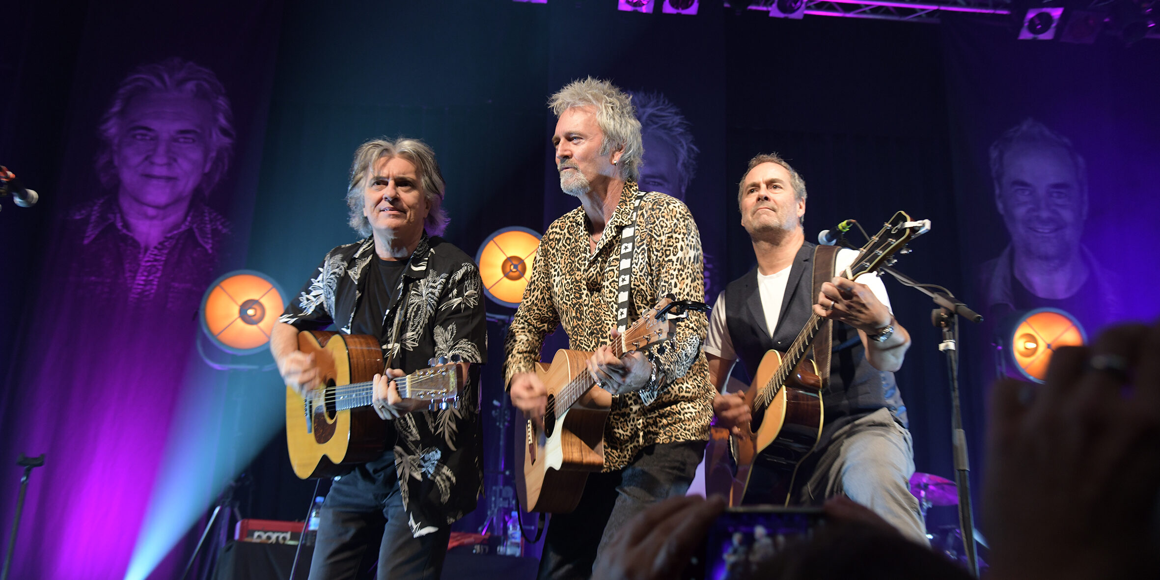 Drei Musiker mit Gitarren auf einer Bühne