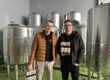 Devin Gerdes (li.) und Daniel Jürck stehen vor silbernen Tanks der Waldstadt-Braumanufaktur.