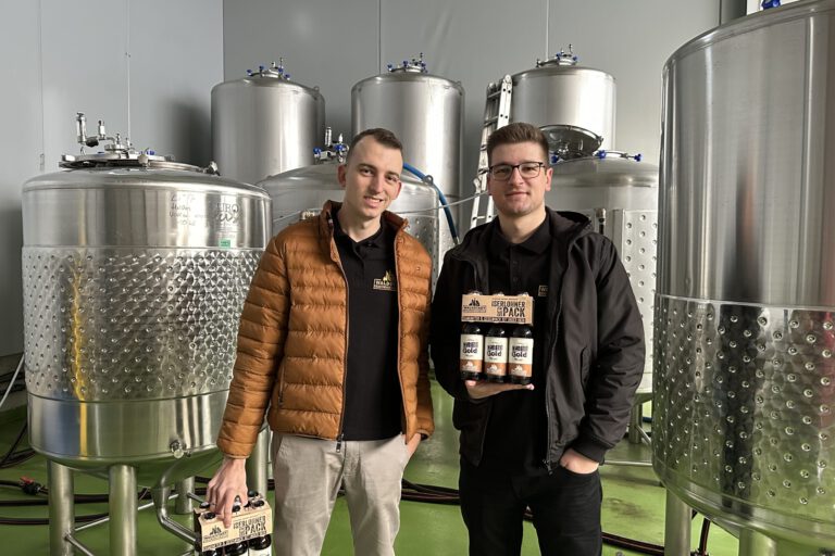 Devin Gerdes (li.) und Daniel Jürck stehen vor silbernen Tanks der Waldstadt-Braumanufaktur.