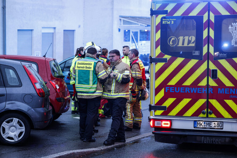 Feuerwehrleute stehen vor einem Wohnhaus, am rechten Bildrand sieht man einen Rettungswagen.