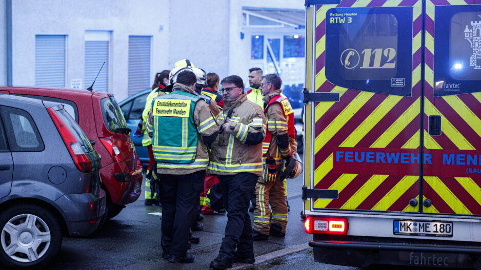 Feuerwehrleute stehen vor einem Wohnhaus, am rechten Bildrand sieht man einen Rettungswagen.