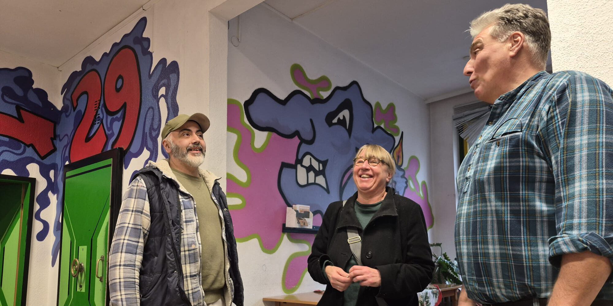 Zwei Männern und eine Frau in einem Raum mit Graffiti an den Wänden.