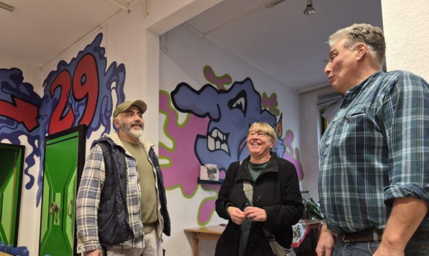 Zwei Männern und eine Frau in einem Raum mit Graffiti an den Wänden.