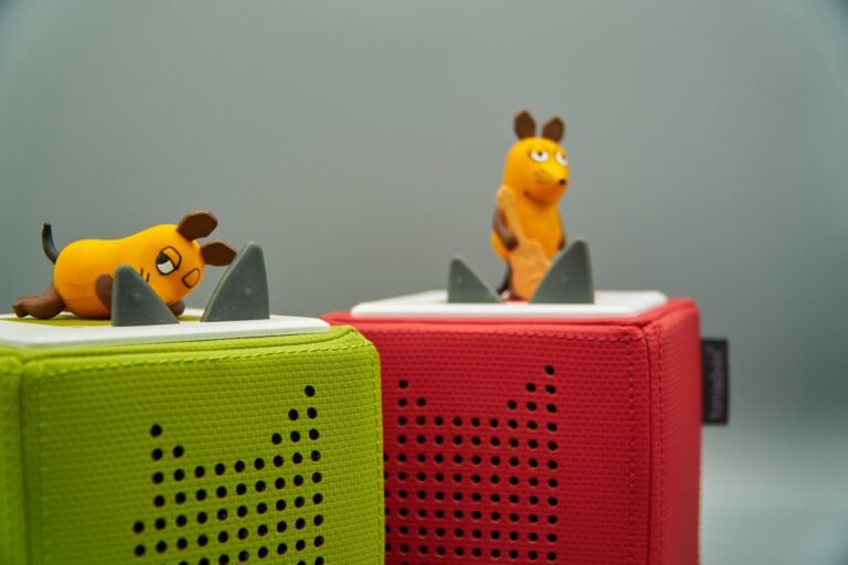 Foto: Markus Distelrath/Pixabay Zwei kleine Spielfiguren in Form der Maus aus der "Sendung mit der Maus" stehen auf bunten, quaderförmigen Lautsprechern (Tonieboxen). Eine Maus liegt auf einem grünen Lautsprecher, die andere steht auf einem roten, beide vor grauem Hintergrund.
