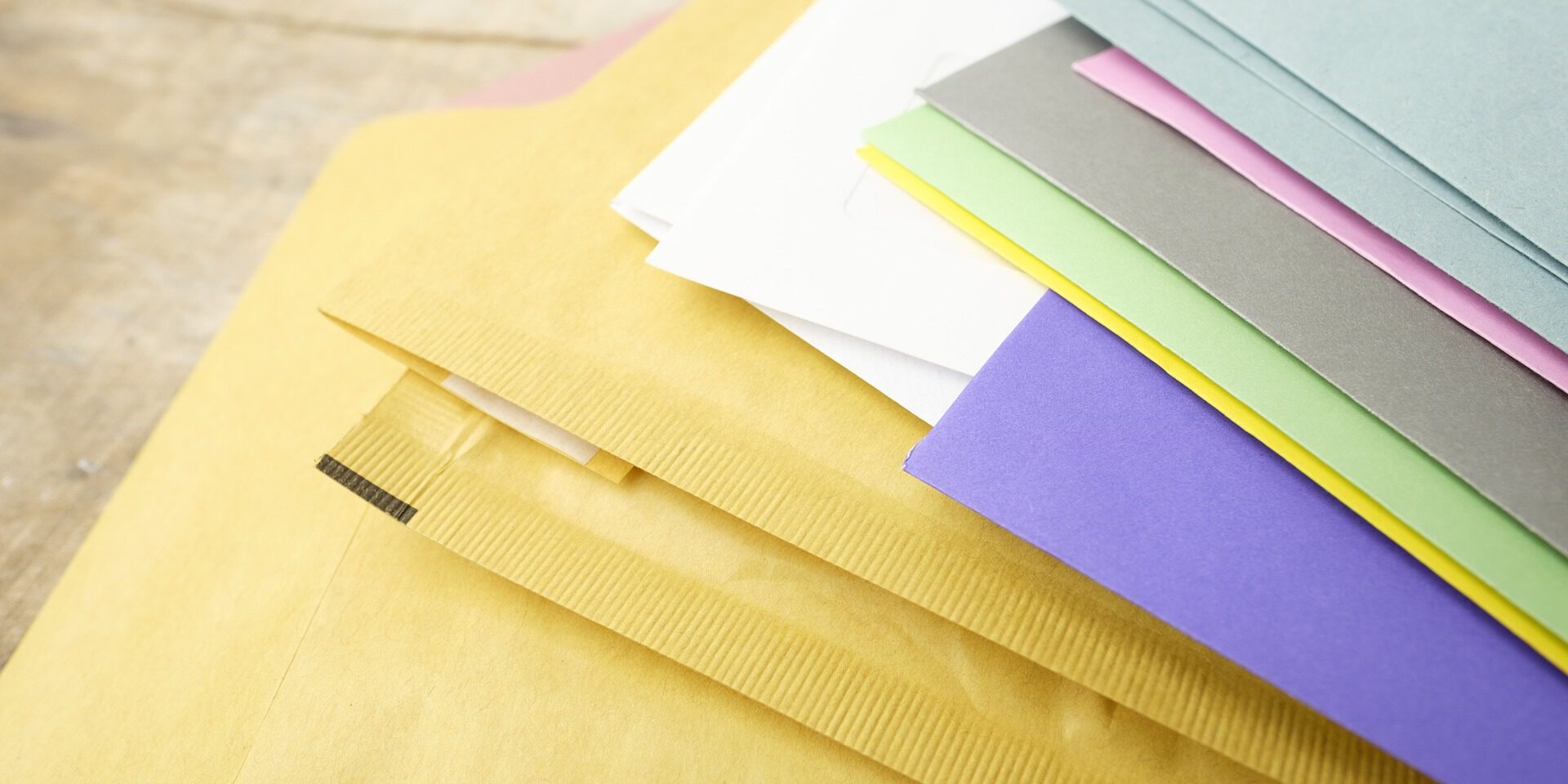 Mehrere farbige Briefumschläge und Papiere liegen übereinander auf einer Tischoberfläche.