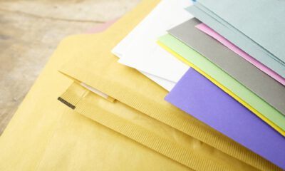 Mehrere farbige Briefumschläge und Papiere liegen übereinander auf einer Tischoberfläche.