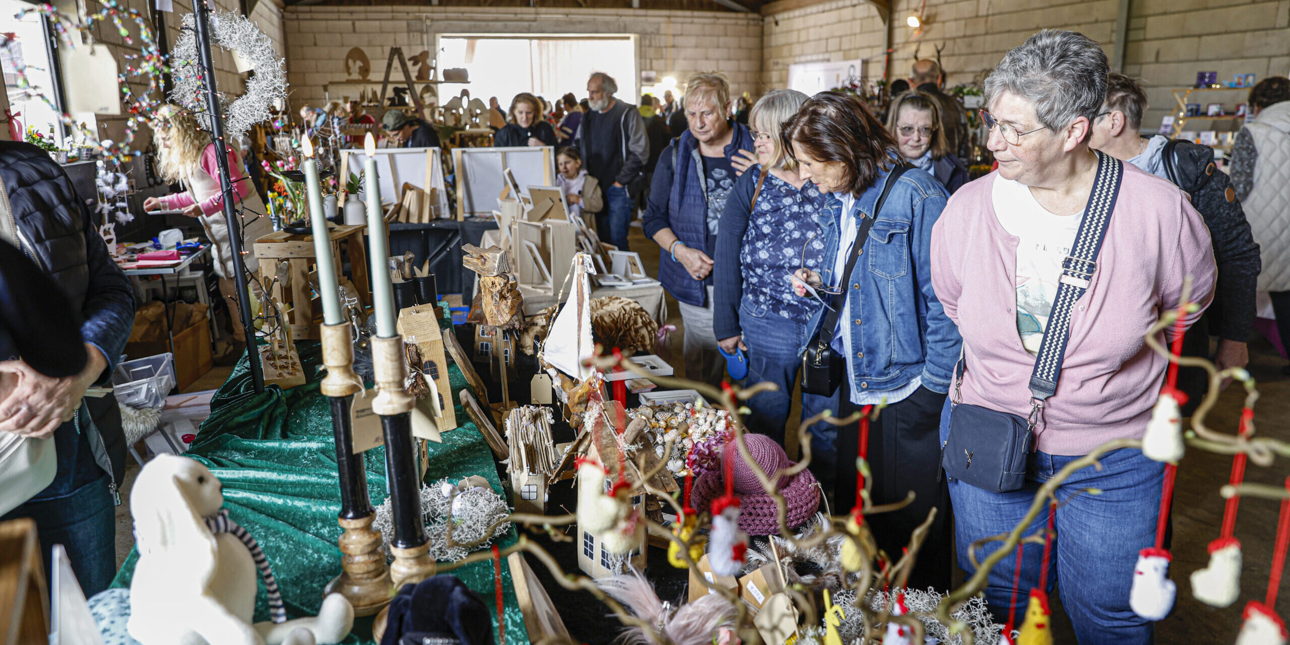Besucherinnen und Besucher schauen sich in einer Scheune an Ständen mit handgemachter Deko, Holzarbeiten und Kunsthandwerk um.