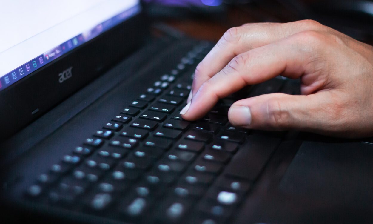 Eine Hand tippt auf der Tastatur eines Laptops, der Bildschirm ist unscharf im Hintergrund zu sehen.
