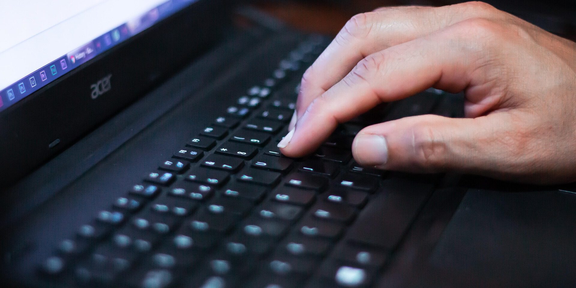 Eine Hand tippt auf der Tastatur eines Laptops, der Bildschirm ist unscharf im Hintergrund zu sehen.