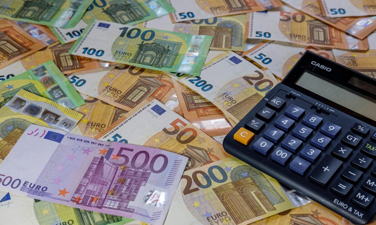 Viele Euro-Banknoten verschiedener Stückelungen liegen ausgebreitet auf einem Tisch, daneben befindet sich ein Taschenrechner.