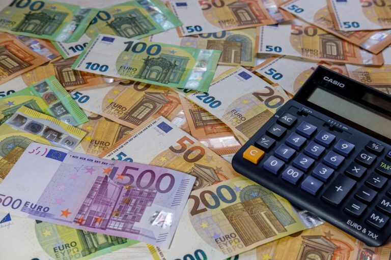 Viele Euro-Banknoten verschiedener Stückelungen liegen ausgebreitet auf einem Tisch, daneben befindet sich ein Taschenrechner.