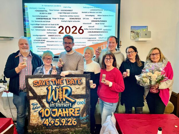 Acht Personen stehen vor einer Präsentationsfolie mit der Jahreszahl 2026 und halten Getränkedosen; davor ein Schild mit „Save the Date – Wir in Ihmert, 10 Jahre“.