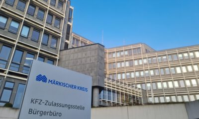 Schild mit der Aufschrift „Märkischer Kreis – KFZ-Zulassungsstelle, Bürgerbüro“ vor einem mehrstöckigen Verwaltungsgebäude.
