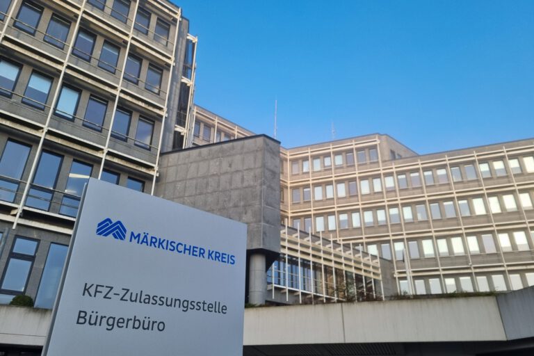Foto: Hannah Heyn/Märkischer Kreis Schild mit der Aufschrift „Märkischer Kreis – KFZ-Zulassungsstelle, Bürgerbüro“ vor einem mehrstöckigen Verwaltungsgebäude.