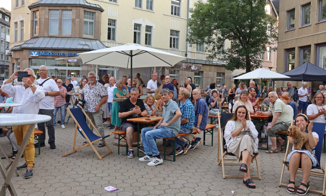 Viele Menschen sitzen und stehen bei einer Veranstaltung auf einem Platz vor der Märkischen Bank und schauen in eine Richtung.