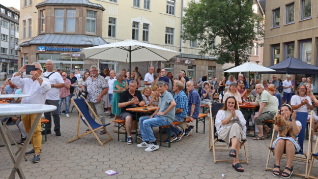 Foto: Stephan Greitzke Viele Menschen sitzen und stehen bei einer Veranstaltung auf einem Platz vor der Märkischen Bank und schauen in eine Richtung.