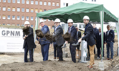 Mehrere Männer mit Schutzhelmen werfen bei einem symbolischen ersten Spatenstich Erde in die Luft.