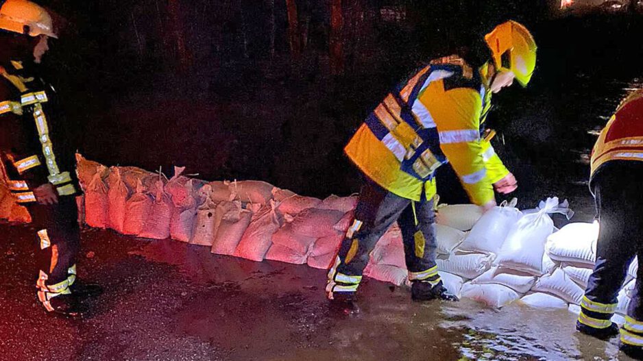 Einsatzkräfte legen nachts Sandsäcke aus, um eine überflutete Straße zu sichern.