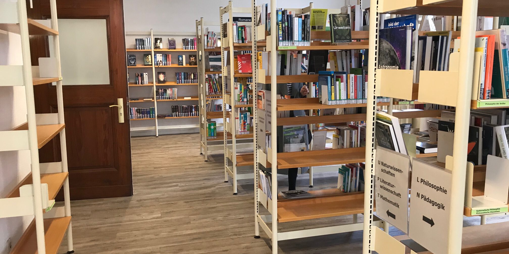 Mehrere Bücherregale mit Sachbüchern und Romanen stehen in einem hellen Raum einer Bibliothek.