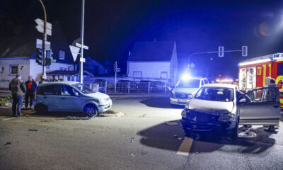 Zwei beschädigte Autos stehen nachts nach einem Unfall auf einer Kreuzung; Polizei und Feuerwehr sind mit Blaulicht vor Ort.