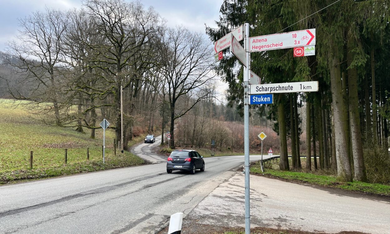 Ein Auto fährt auf einer Landstraße an einer Kreuzung mit Wegweisern Richtung Altena und Hegenscheid vorbei.