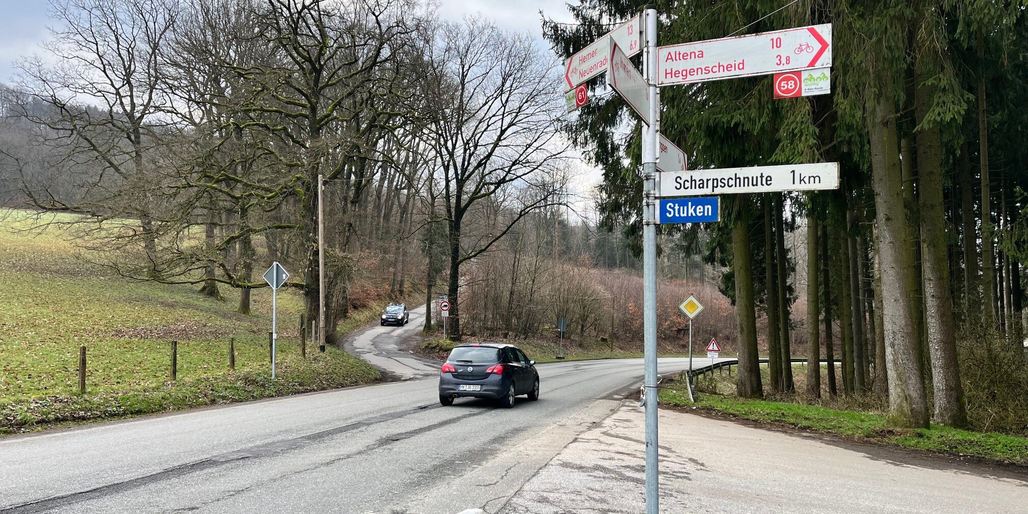 Ein Auto fährt auf einer Landstraße an einer Kreuzung mit Wegweisern Richtung Altena und Hegenscheid vorbei.