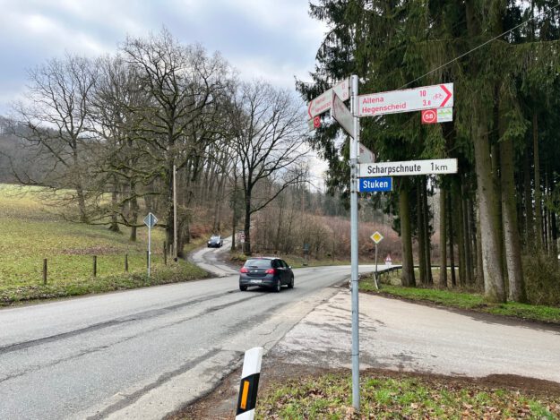 Ein Auto fährt auf einer Landstraße an einer Kreuzung mit Wegweisern Richtung Altena und Hegenscheid vorbei.