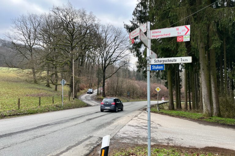 Ein Auto fährt auf einer Landstraße an einer Kreuzung mit Wegweisern Richtung Altena und Hegenscheid vorbei.