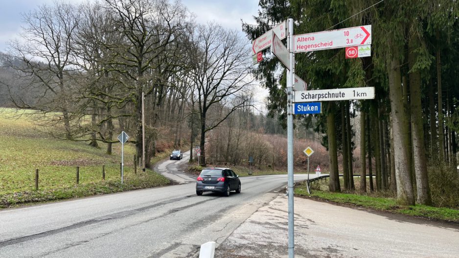 Ein Auto fährt auf einer Landstraße an einer Kreuzung mit Wegweisern Richtung Altena und Hegenscheid vorbei.