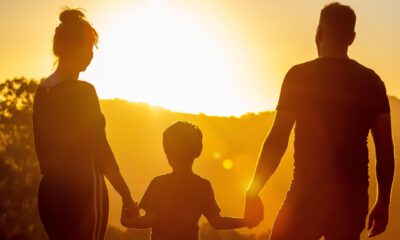 Zwei Erwachsene und ein Kind halten sich bei Sonnenuntergang an den Händen und schauen in die Ferne.