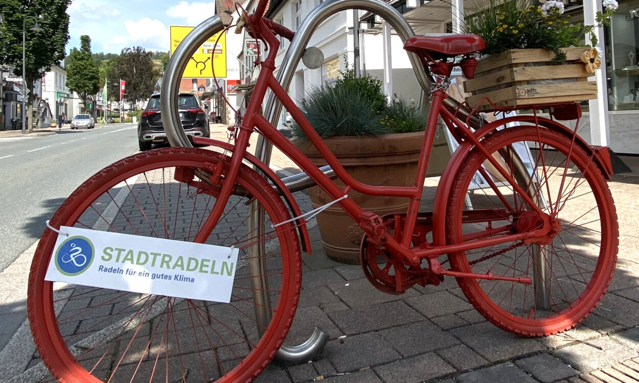 Ein rot lackiertes Fahrrad steht als Deko in der Innenstadt, am Rahmen hängt ein Schild mit der Aufschrift „Stadtradeln – Radeln für ein gutes Klima“.