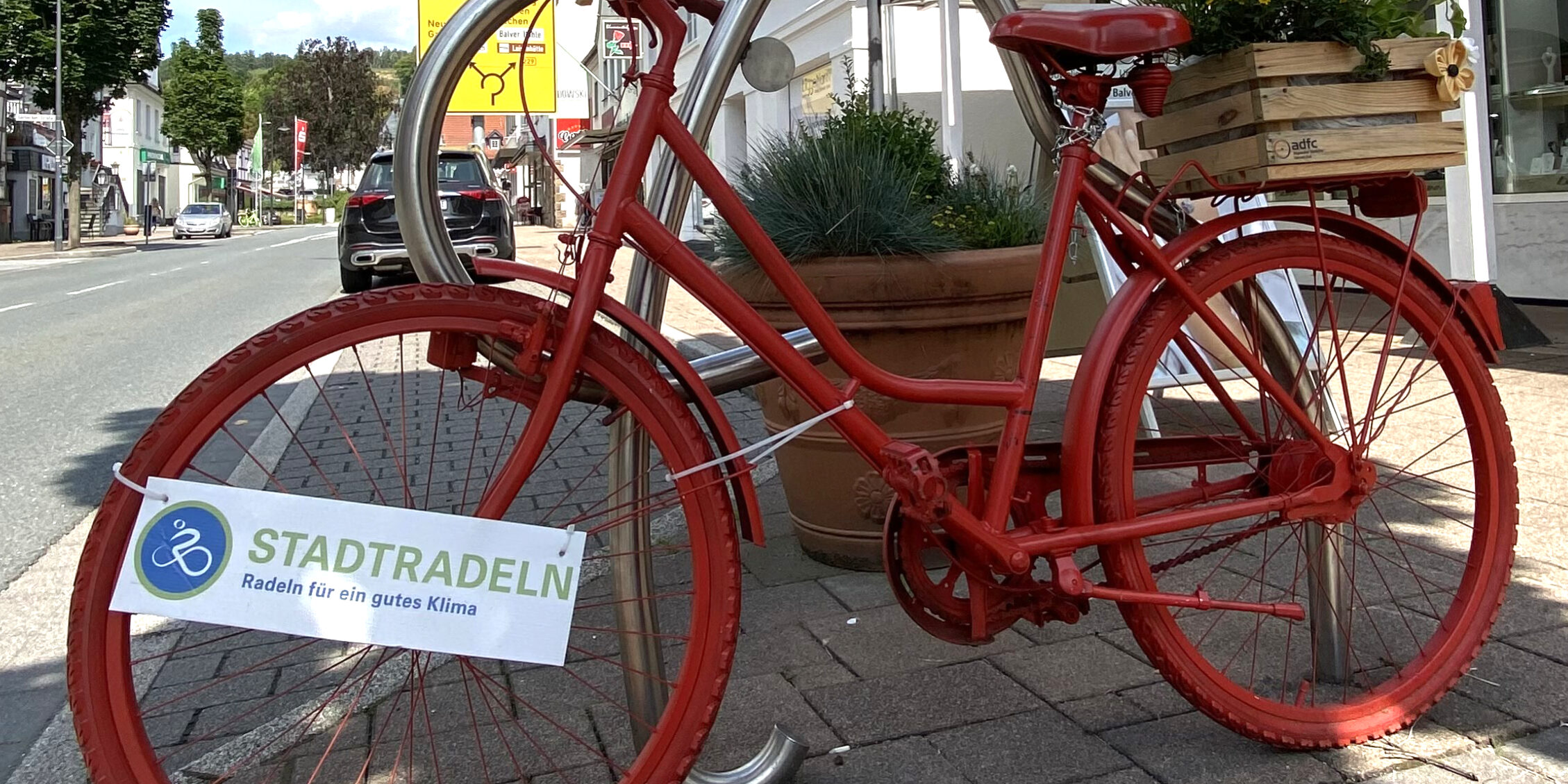 Ein rot lackiertes Fahrrad steht als Deko in der Innenstadt, am Rahmen hängt ein Schild mit der Aufschrift „Stadtradeln – Radeln für ein gutes Klima“.