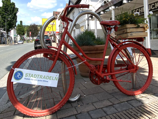 Ein rot lackiertes Fahrrad steht als Deko in der Innenstadt, am Rahmen hängt ein Schild mit der Aufschrift „Stadtradeln – Radeln für ein gutes Klima“.