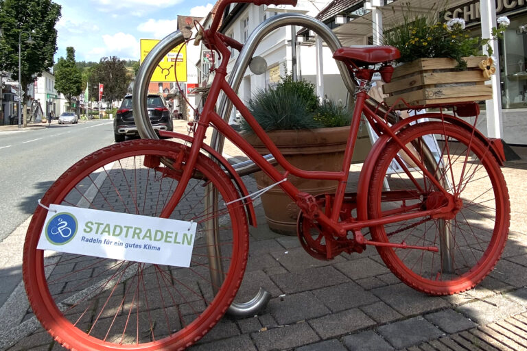 Ein rot lackiertes Fahrrad steht als Deko in der Innenstadt, am Rahmen hängt ein Schild mit der Aufschrift „Stadtradeln – Radeln für ein gutes Klima“.