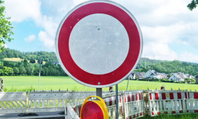Ein rundes Verkehrsschild „Durchfahrt verboten“ steht vor einer abgesperrten Straße mit Baustellenbarrieren in ländlicher Umgebung.