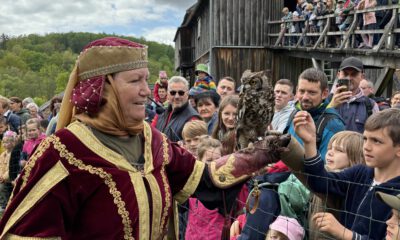 Frau in historischer Kleidung präsentiert eine Eule auf ihrer Hand vor einer Gruppe von Kindern und Erwachsenen bei einer Vorführung im Freien.