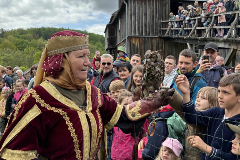 Frau in historischer Kleidung präsentiert eine Eule auf ihrer Hand vor einer Gruppe von Kindern und Erwachsenen bei einer Vorführung im Freien.