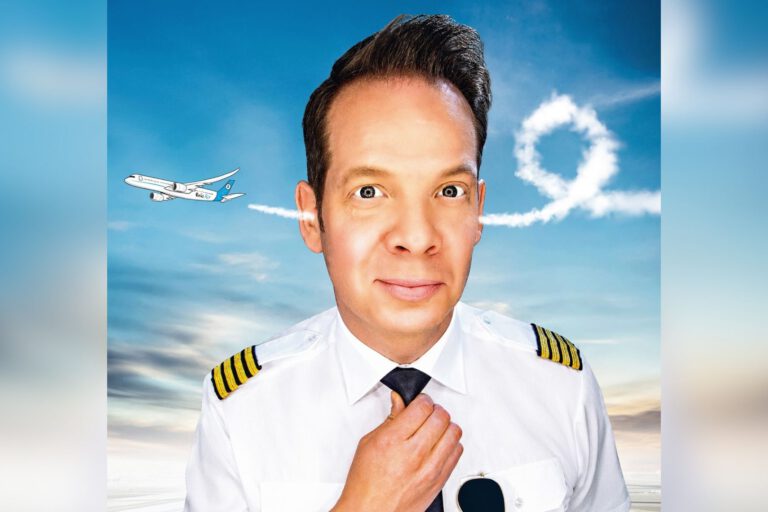 Ein Mann in Pilotenuniform schaut frontal in die Kamera und richtet seine Krawatte, während im Hintergrund ein Flugzeug am Himmel eine Schleife aus Kondensstreifen zieht.