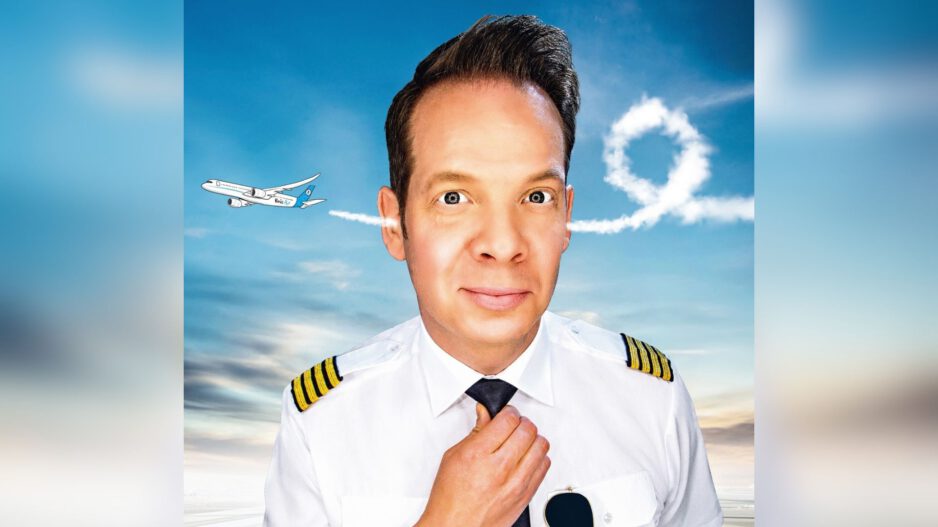 Ein Mann in Pilotenuniform schaut frontal in die Kamera und richtet seine Krawatte, während im Hintergrund ein Flugzeug am Himmel eine Schleife aus Kondensstreifen zieht.