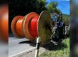 Traktor transportiert große Kabeltrommeln mit orangefarbenen Leitungen am Straßenrand entlang.