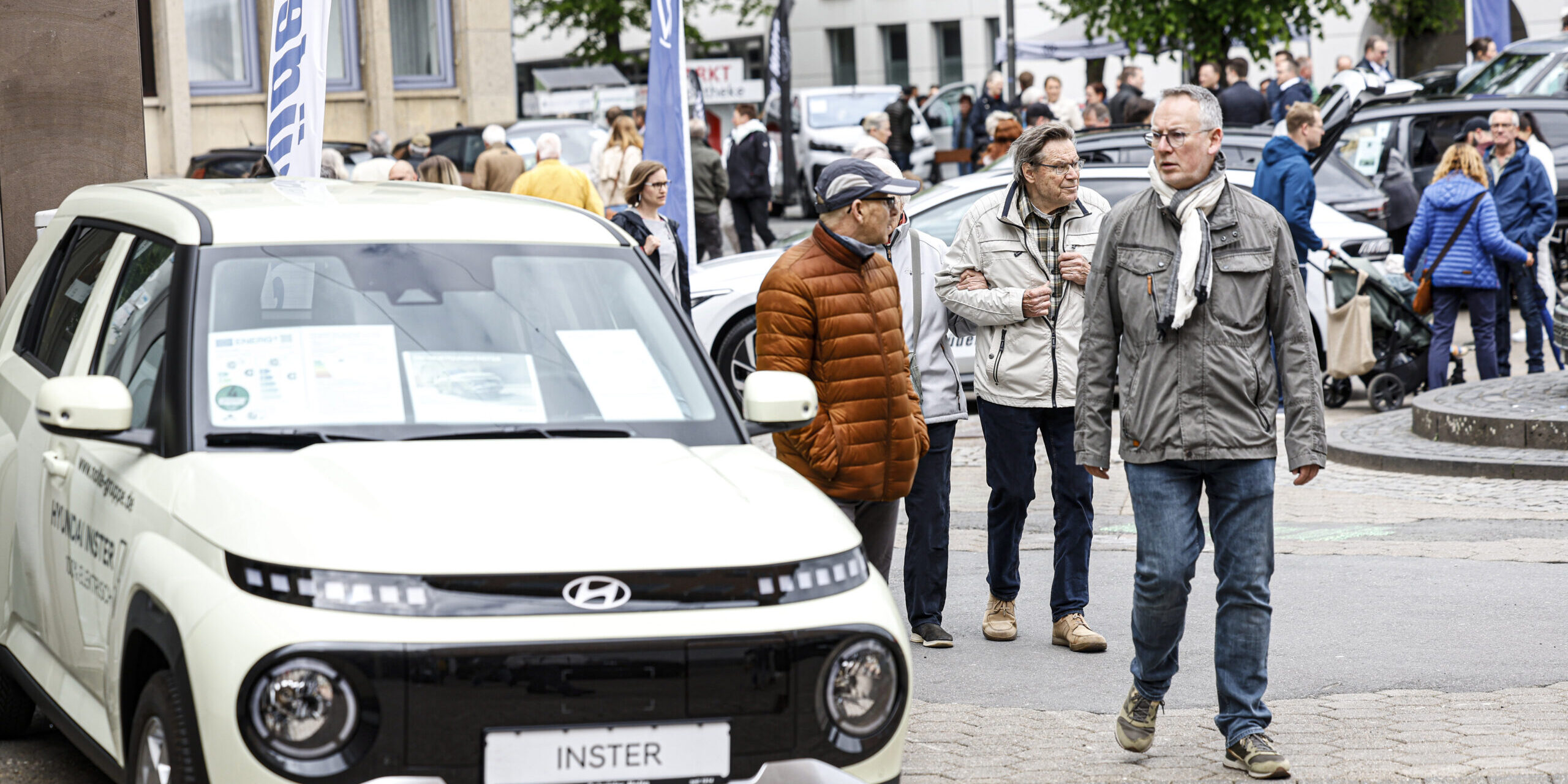 Menschen besuchen eine Autoschau in der Innenstadt und betrachten ausgestellte Fahrzeuge, im Vordergrund ein Hyundai-Modell.
