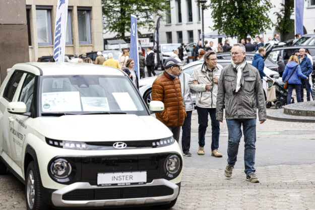 Menschen besuchen eine Autoschau in der Innenstadt und betrachten ausgestellte Fahrzeuge, im Vordergrund ein Hyundai-Modell.