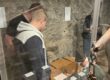 Mehrere Menschen betrachten in einem historischen Kellerraum eine Ausstellung mit alten Gegenständen hinter Glasvitrinen und Steinmauern im Hintergrund.