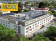 Luftaufnahme einer modernen Wohnanlage mit mehreren Gebäudeteilen, begrünten Außenflächen, Parkplätzen und einer Dachterrasse inmitten eines Wohngebiets. Oben links steht ein Hinweis, dass es sich um eine Anzeige handelt.
