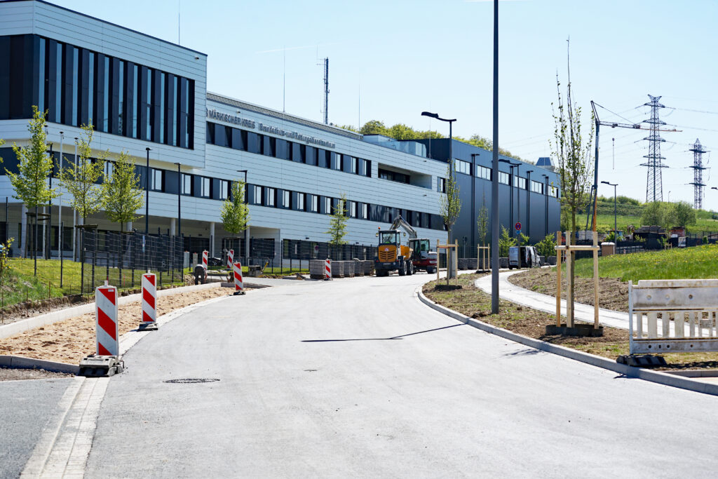 Eine neu gebaute Straße mit jungen Bäumen am Straßenrand und einem weißen Firmengebäude im Hintergrund.