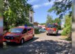 Mehrere Einsatzfahrzeuge von Feuerwehr und Polizei stehen an einer schmalen Straße zwischen Bäumen und Wohnhäusern.